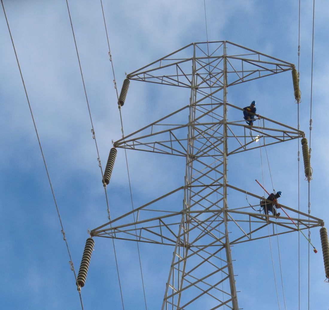 Técnicos de OYM trabajando sobre las crucetas de una torre de transmisión